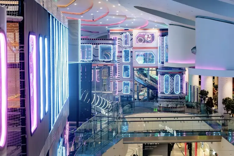 Вид со стороны ТРЦ на парк развлечений в ТРЦ Океания: высокие лабиринты с неоновой подсветкой.