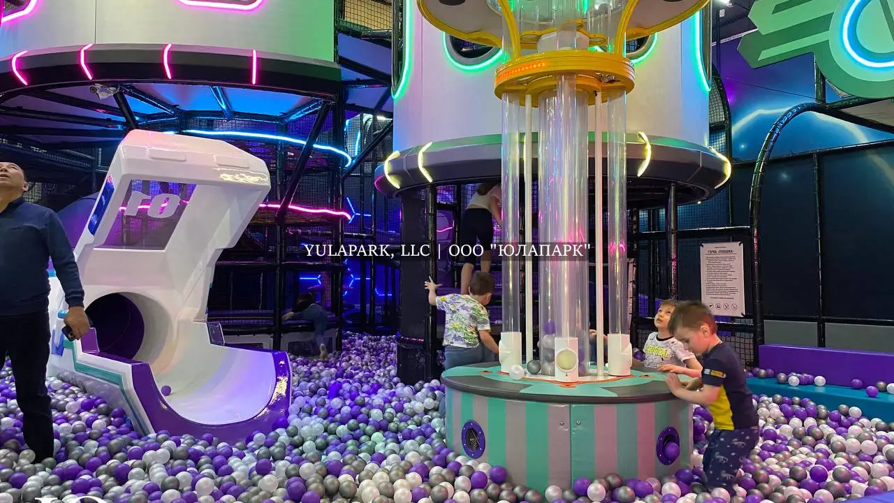 Фиолетовые и белые шарики в сухом бассейне, детская горка в виде змея и динозавтра с подсветкой, сухой фонтан с шарами и большой детский лабиринт в развлекательном центре для детей.