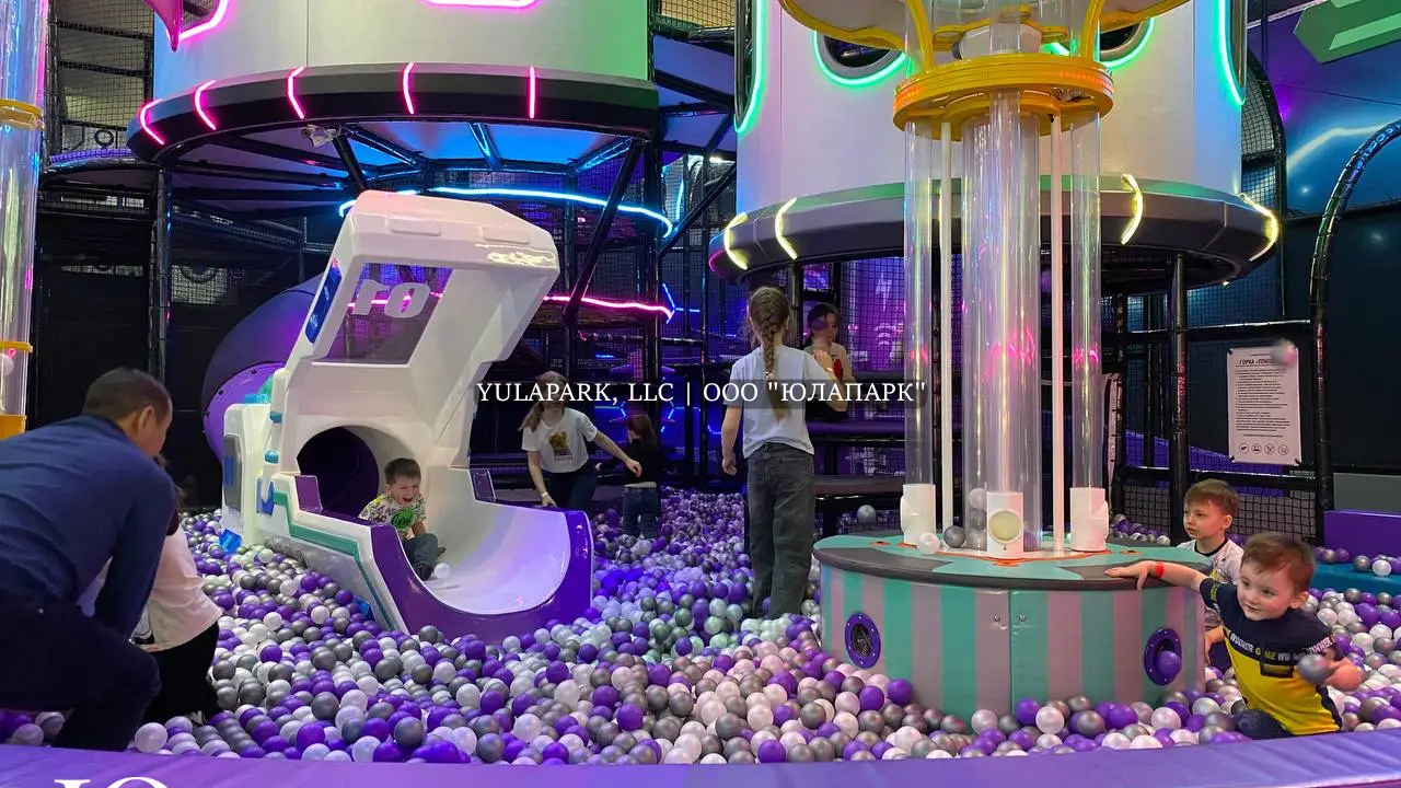 Фиолетовые и белые шарики в сухом бассейне, горка в виде змея и динозавтра, сухой фонтан с шарами и большой детский лабиринт в развлекательном центре для детей.