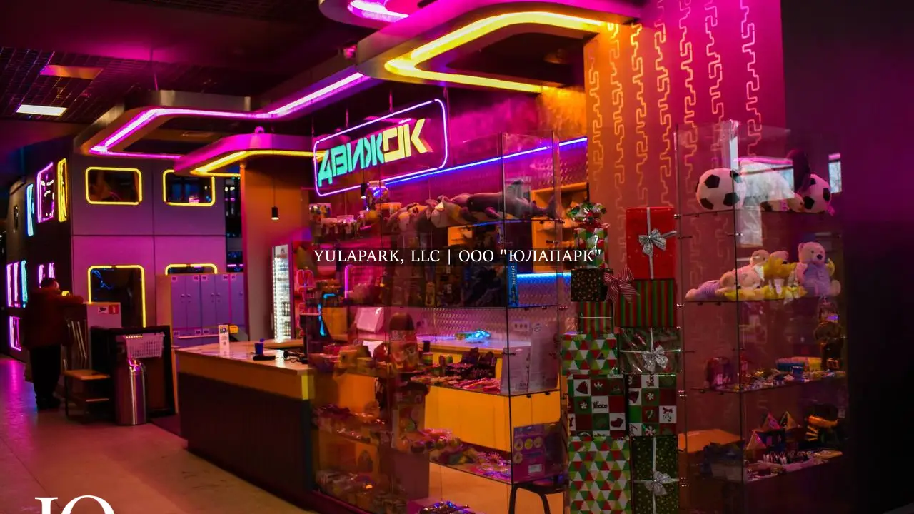 Вход и входная группа в детский активити-парк Движок в Омске с неоновой розовой, синей и желтой подсветками, большим ресепшеном и витриной с подарками и сладостями.
