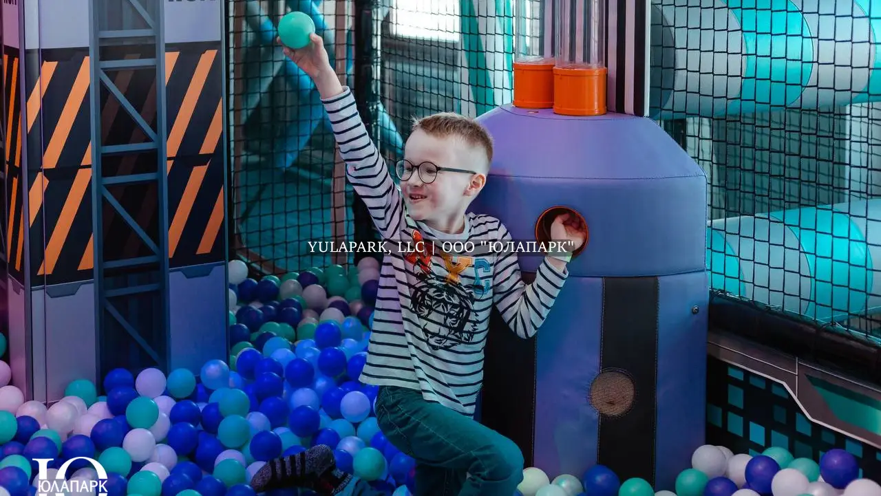 Мальчик играет с фонтаном сухих шаров в сухом детском бассейне с фиолетовыми, голубыми и белыми шариками в детском парке Движок в Омске.