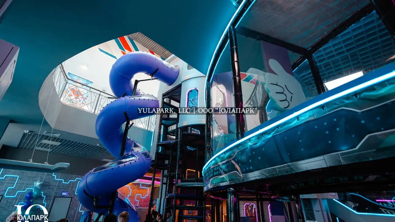 Высокая башня в виде космического корабля с неоновой подсветкой в детском активити-парке, с высокой закрученной пластиковой горкой в активити-парке Движок в Омске.