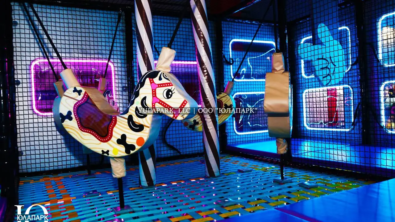 Вид на качели в виде зебры и других животных внутри лабиринта с неоновой подсветкой и большими окнами в активити-парке Движок.