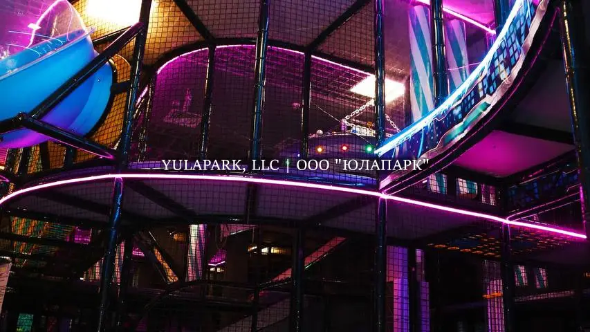 Вид на высокий многоэтажный лабиринт на мост небольшие окна с неоновой подсветкой и пуфиками внизу в детском активити-парке Движок.