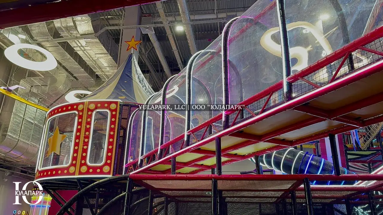 Длинный прозрачный мост с неоновой подсветкой и красной башней в виде купола цирка в детском развлекательном парке Флик Фляк.