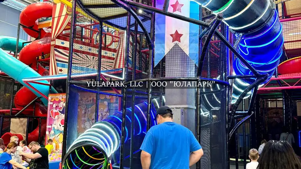 Яркая пластиковая горка с неоновой подсветкой в парке в стиле цирка Фляк Фляк.