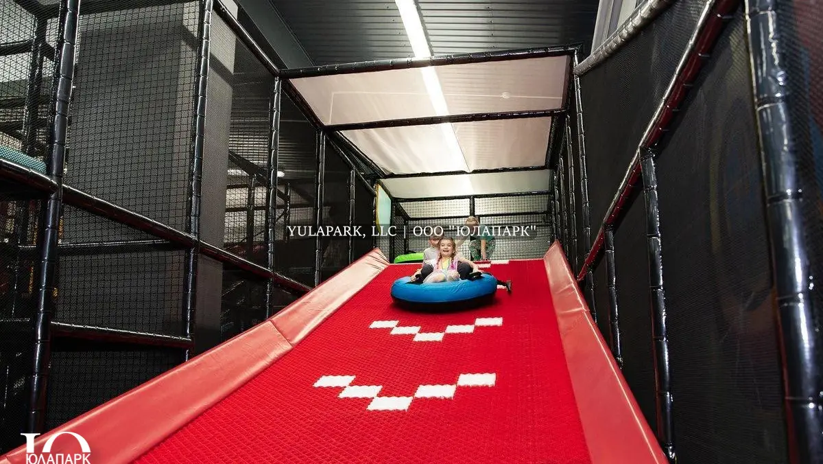 Красная горка для тюбинга для детей, по которой скатывается на игровой ватрушке ребенок в детском парке развлечений.