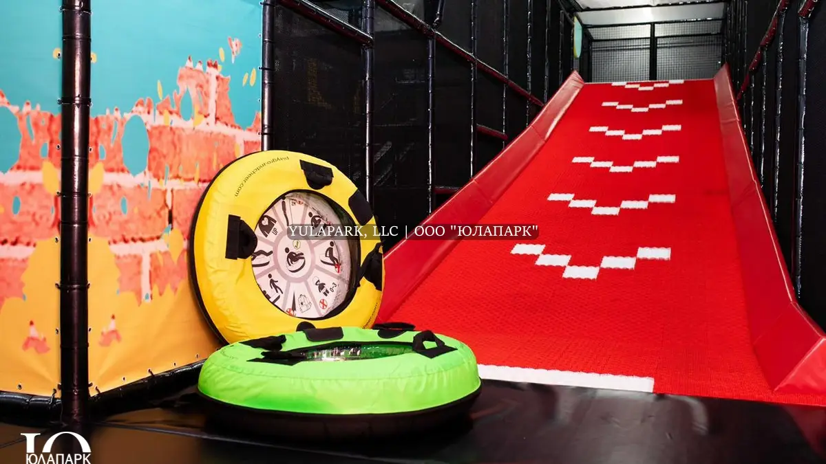 Красная горка для тюбинга для детей, по которой скатывается на игровой ватрушке ребенок в детском парке развлечений.