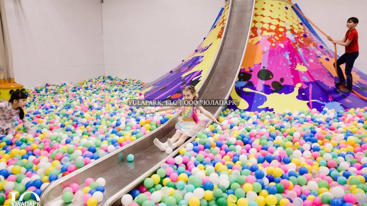 Вулкан для детей сол стальной открытой горкой в большом разноцветном сухом бассейне в игровой комнате для детей.